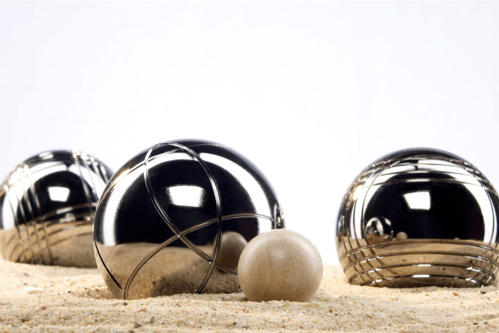 3 boules de pétanque posées sur du sable avec le cochonnet devant