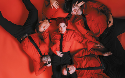 Sur l’image, on voit les cinq membres du groupe Superbus alignés côte à côte. La chanteuse, Jennifer Ayache, est au centre, vêtue de noir avec une pose assurée. Les autres membres, également habillés en noir ou en tons sombres, adoptent des attitudes cool et détendues. Le fond est neutre, sombre, mettant en valeur leur style rock. L’image dégage une ambiance moderne et énergique, fidèle à l’univers du groupe.